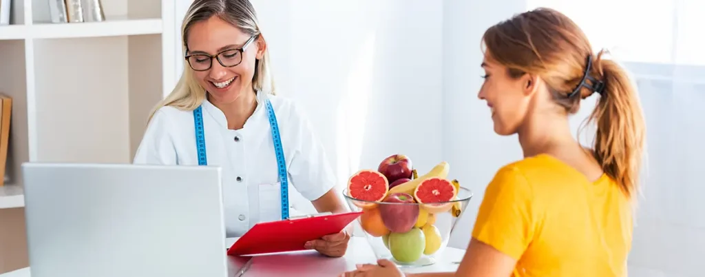 Dietitian consulting with a client beside a laptop and bowl of fresh fruit.